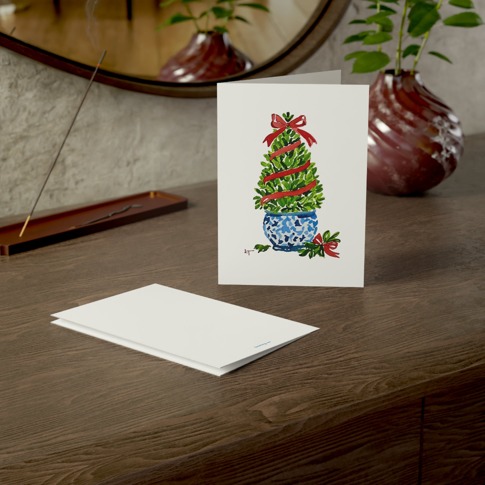Boxwood Christmas topiary with red ribbon in blue and white chinoiserie pot watercolor Christmas card on a wooden dresser with envelope