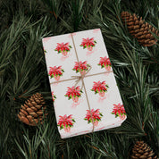 Poinsettia wrapping paper with red watercolor poinsettias on white by Laura Trevey, wrapped gift on evergreen branches with pinecones