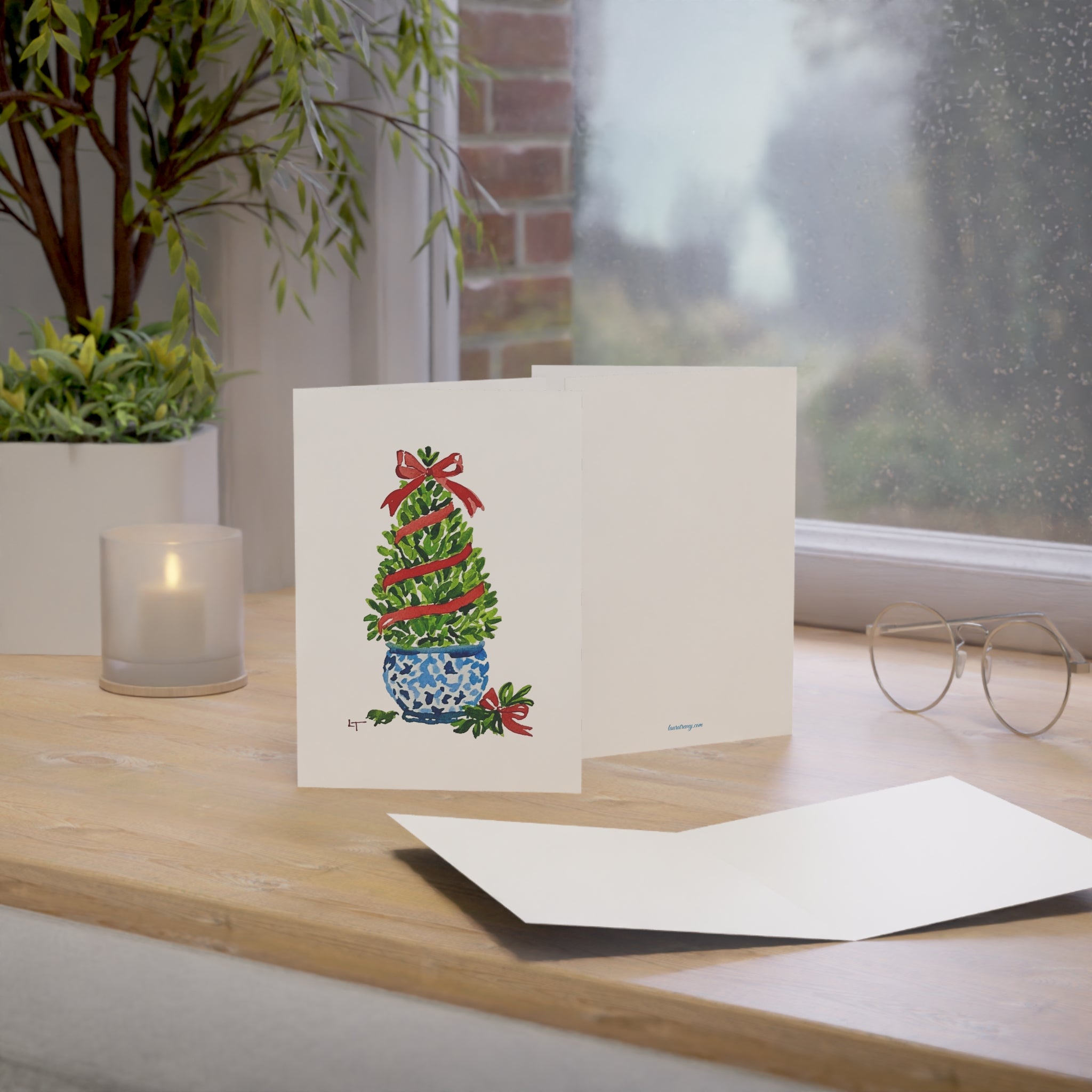 Boxwood Christmas topiary with red ribbon in blue and white chinoiserie pot watercolor holiday card on a windowsill desk with envelope