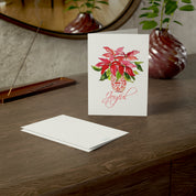 Joyful red poinsettia watercolor Christmas card on a wooden dresser with envelope