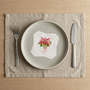 Holiday table place setting with Laura Trevey Joyful poinsettia paper napkins on a linen placemat