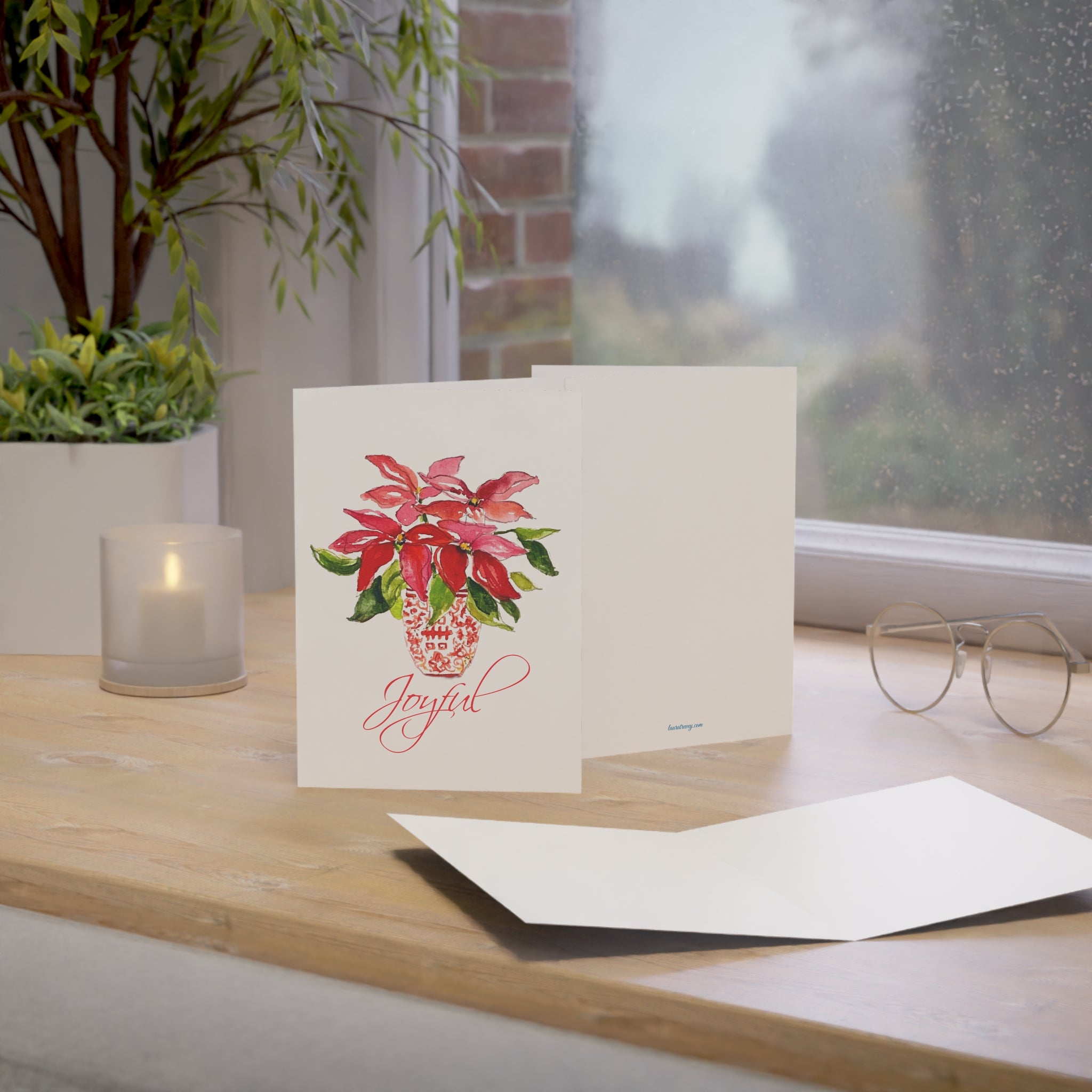 Joyful red poinsettia watercolor holiday card on a windowsill desk with envelope
