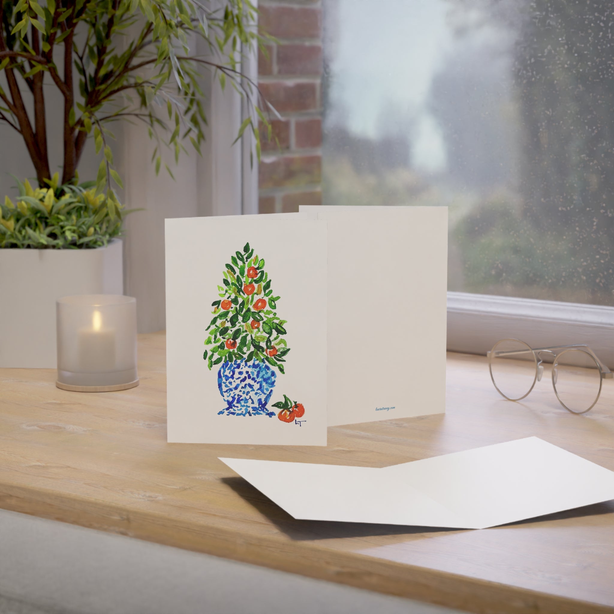 Orange tree Christmas topiary in blue and white chinoiserie pot watercolor holiday card on a windowsill desk with envelope