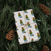 Christmas topiary wrapping paper with watercolor boxwood trees in blue and white chinoiserie pots by Laura Trevey, wrapped gift on evergreen branches with pinecones