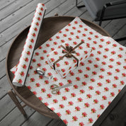 Poinsettia wrapping paper with red watercolor poinsettias on white by Laura Trevey, full sheet with a wrapped gift on a wooden table