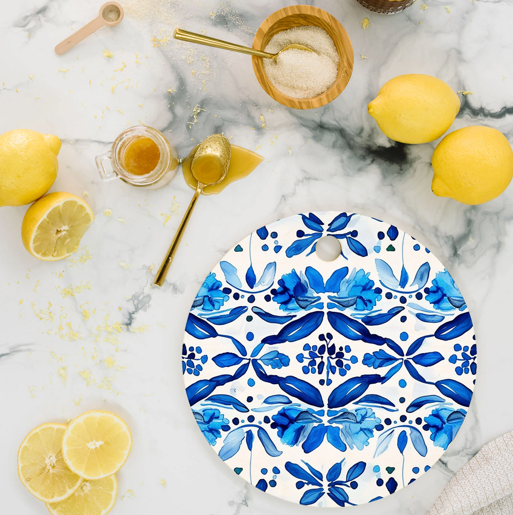 Decorative blue and white cutting board with Spanish tile inspired pattern on a marble surface with lemons and honey.