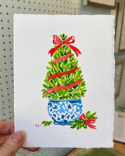 Laura Trevey holding her original boxwood topiary watercolor with red bow in her Richmond, VA studio