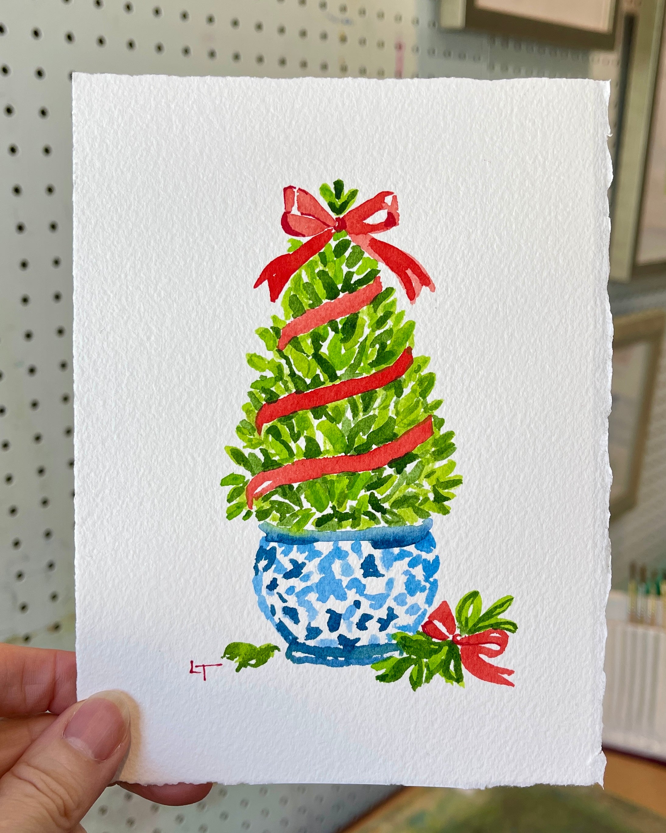 Laura Trevey holding her original boxwood topiary watercolor with red bow in her Richmond, VA studio