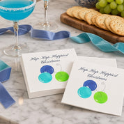 Hap Hap Happiest Christmas Blue Cocktail Napkins | Watercolor Ornament Paper Napkins – Blue Hap Hap Happiest Christmas cocktail napkins by Laura Trevey on white marble with icy blue cocktails, a chinoiserie bowl of ornaments and periwinkle ribbon