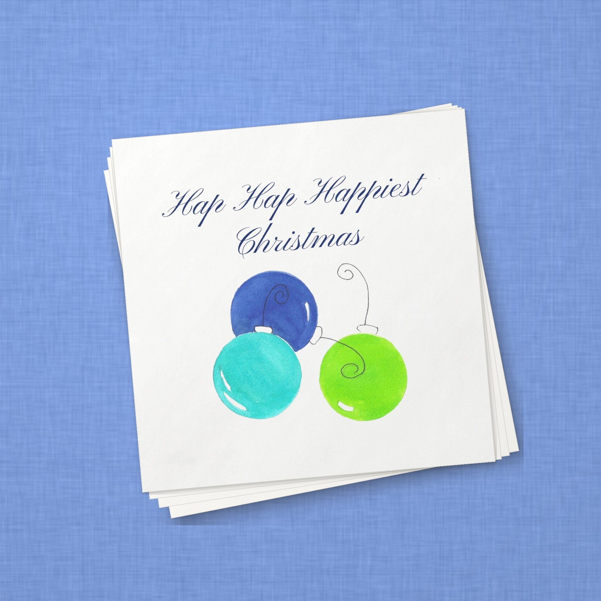 Hap Hap Happiest Christmas Blue Cocktail Napkins | Watercolor Ornament Paper Napkins – stack of cocktail napkins on periwinkle blue linen