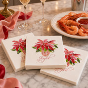 Joyful Poinsettia Christmas Cocktail Napkins | Watercolor Holiday Paper Napkins – Joyful poinsettia Christmas cocktail napkins by Laura Trevey on a white marble counter with champagne flutes, shrimp cocktail and pink and red ribbon